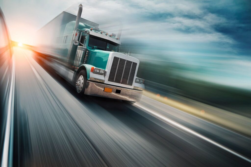 Milford Truck Accident Lawyer features photo of green truck speeding down a new hampshire highway away from a sunset with the background blurred to represent speed, milford car accident services